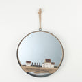 Round mirror with a decorative frame hanging on a white wall, reflecting a scenic view.